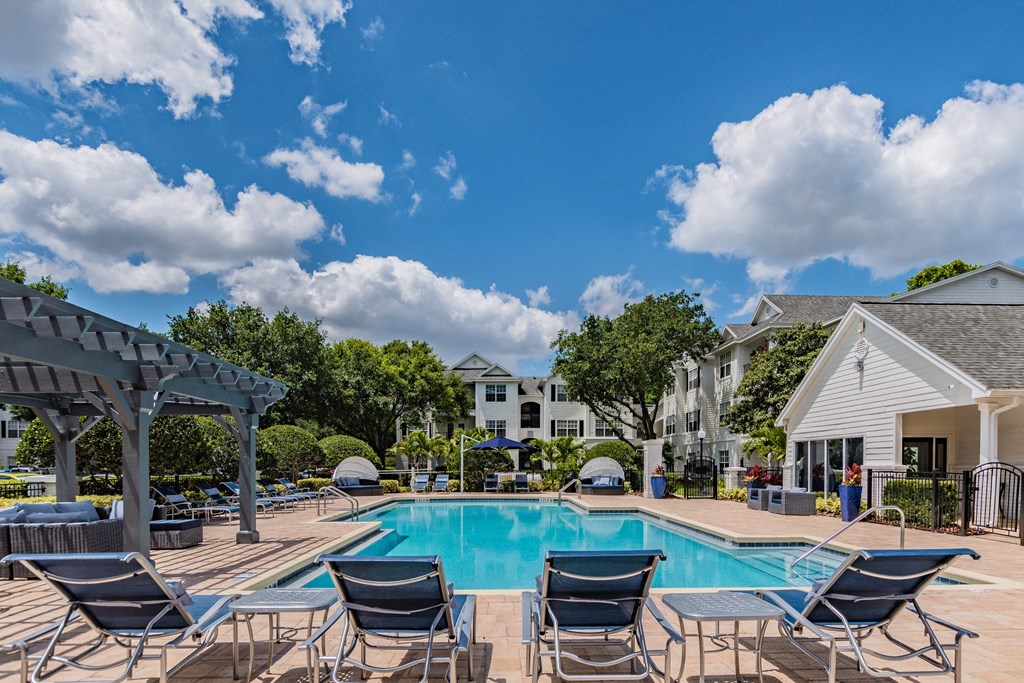 Apartments Near Baldwin Park, FL - Infinity off Baldwin Park - Outdoor Pool Area with Lounge Seating, Covered Seating, with Surrounding Trees and Shrubbery