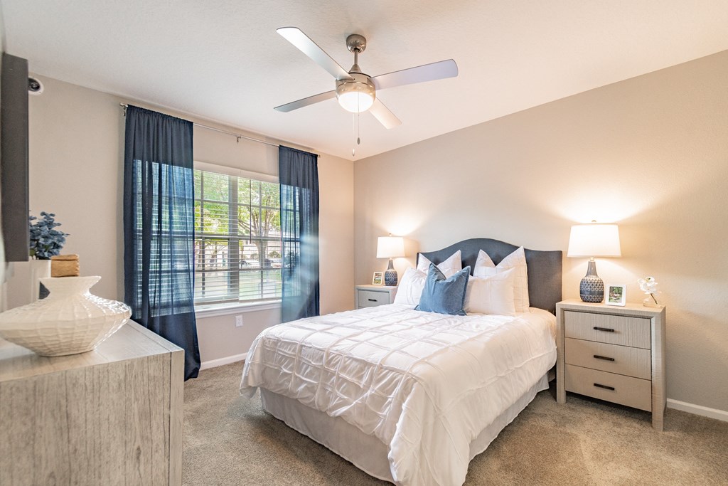 A bedroom with a large bed, ceiling fan and window.