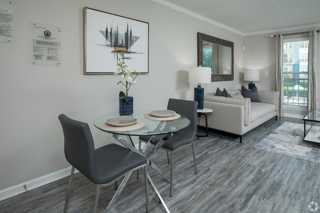 a dining area with a glass table and chairs and a couch in the background