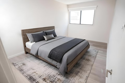A bed with a wooden headboard and grey bedding is in a room with a rug on the floor.