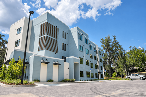 A modern building with a white and blue exterior and a parking lot in front.