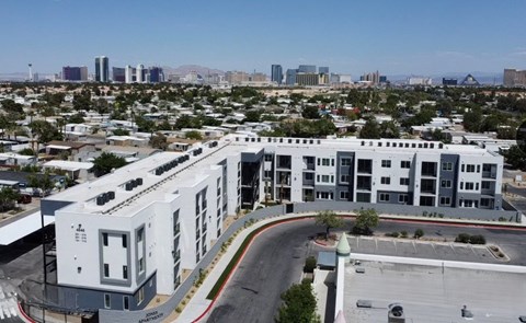 A modern white building with a parking lot in front and a cityscape in the background.