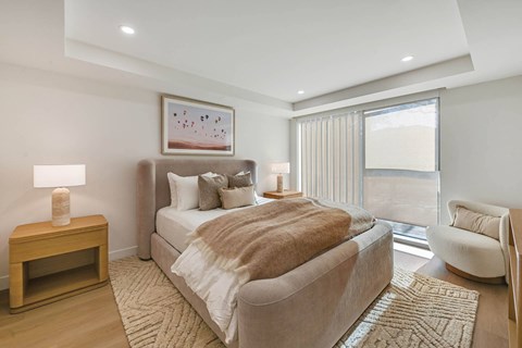 A bedroom with a large bed and a small table with a lamp on it.