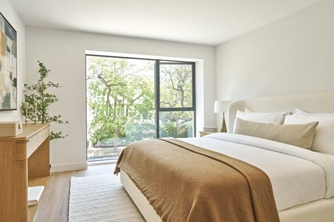 A bedroom with a large bed and a view of trees outside the window.