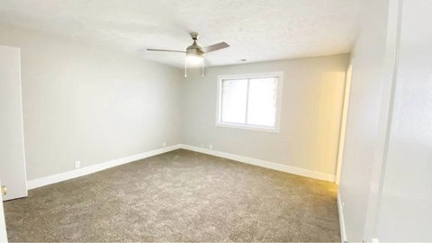 A room with a carpeted floor, a ceiling fan, and a window.