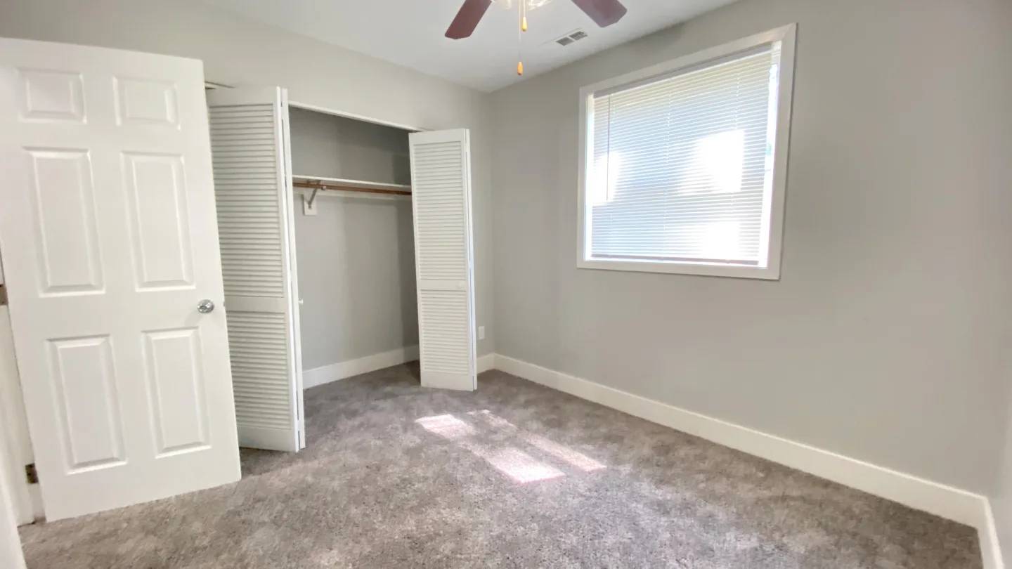 A room with a white door, a window with blinds, and a ceiling fan.
