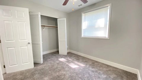 A room with a white door, a window with blinds, and a ceiling fan.