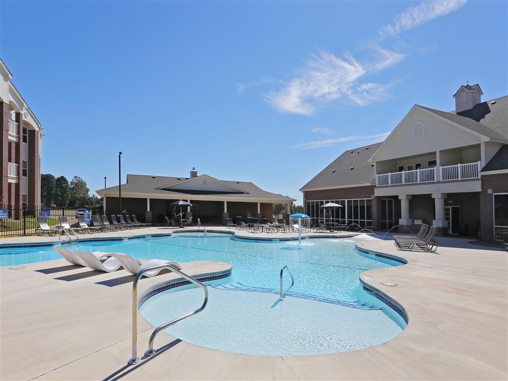 A large swimming pool with a slide and sun loungers in front of a building.
