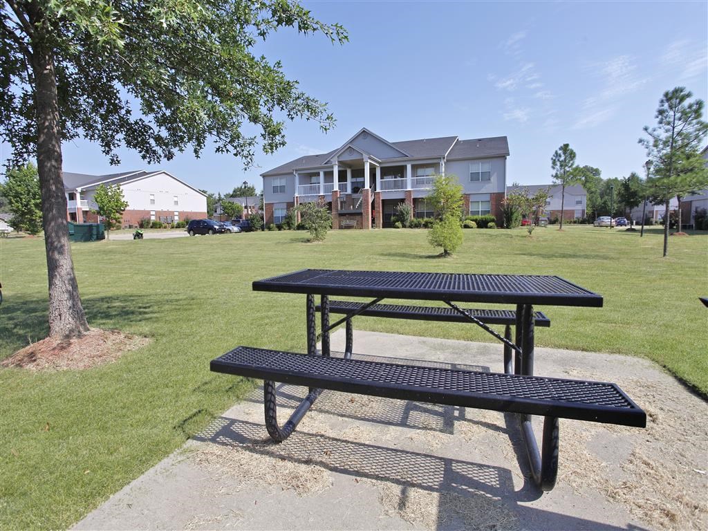 A black picnic table and bench in front of a grassy area with apartment buildings in the background.