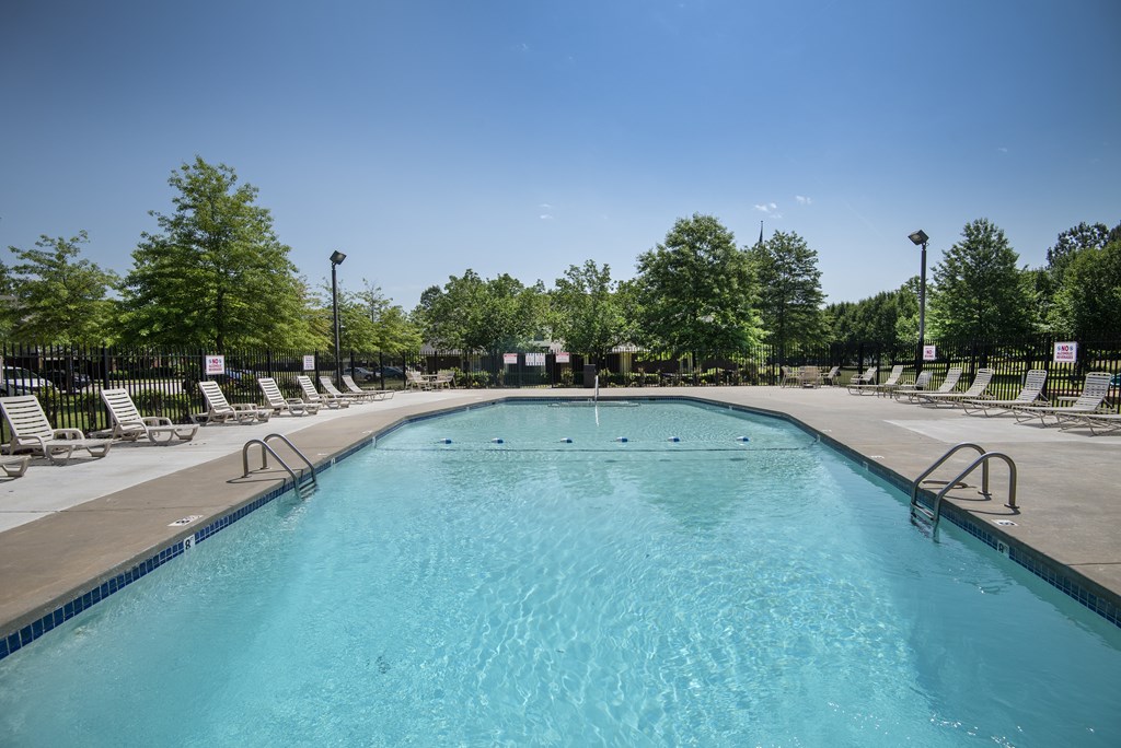 A large outdoor swimming pool surrounded by lounge chairs and trees.