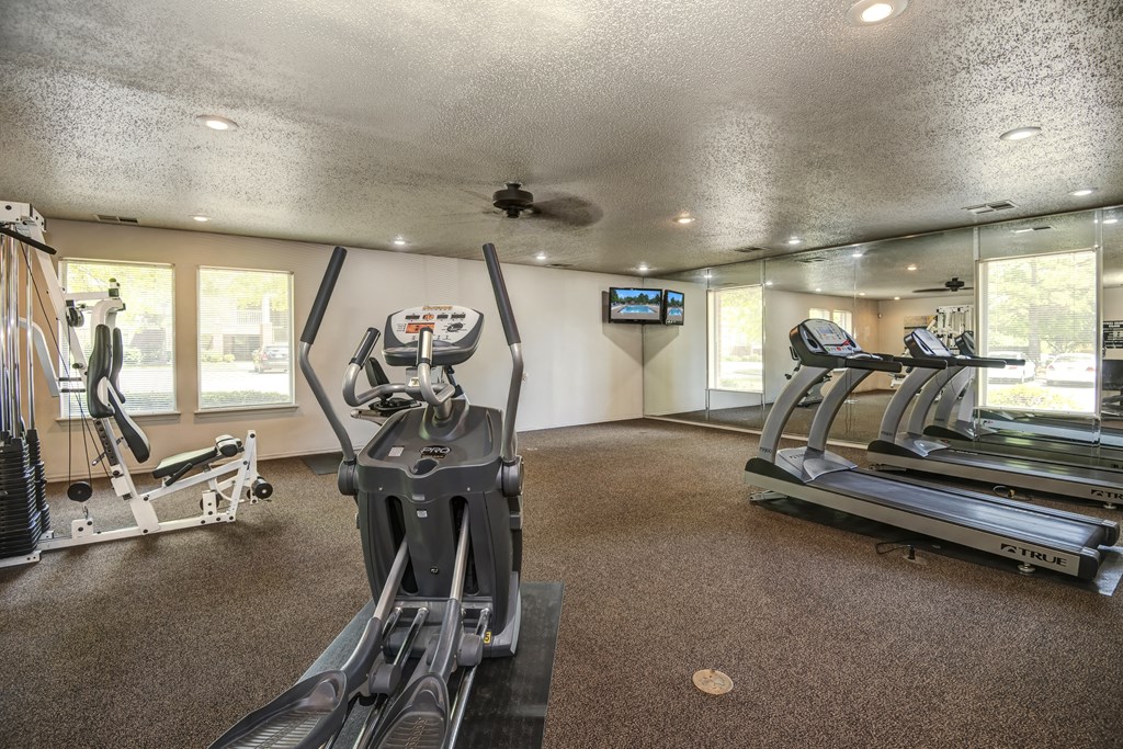 A spacious gym with treadmills, elliptical machines, and a television.