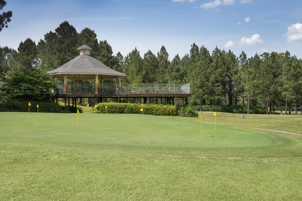 A gazebo sits on a golf course surrounded by trees.