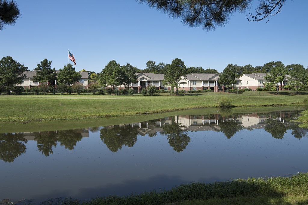 A pond in front of a row of houses with a flag flying in the background.