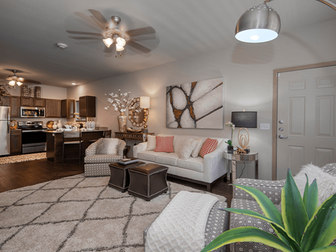 a living room with a ceiling fan and a kitchen in the background