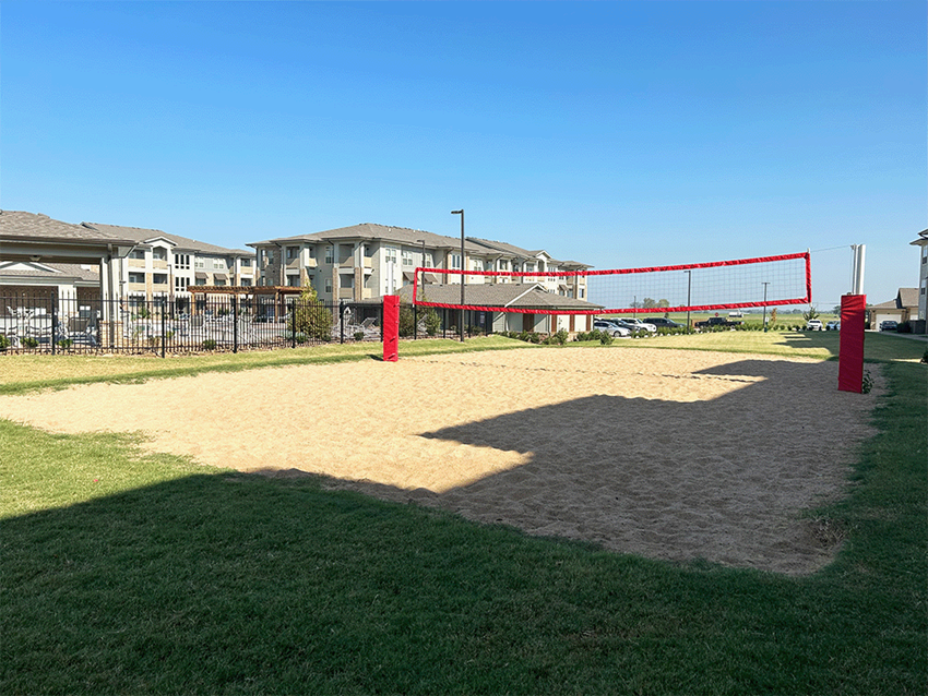 a sandy volleyball court in a grassy area with houses in the background
