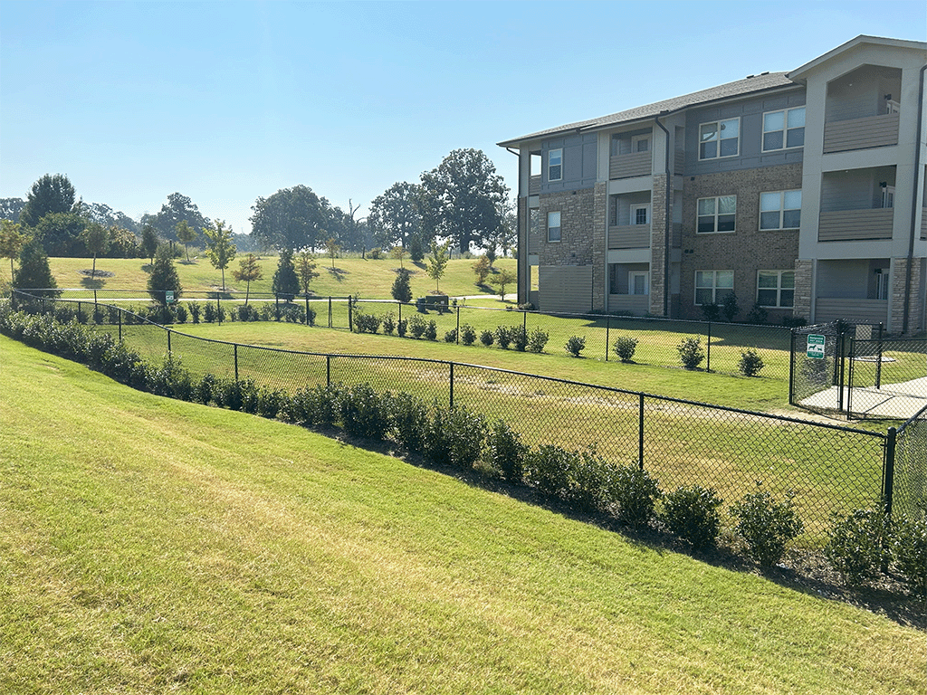 an apartment building on a grassy hill with a chain link fence in front of it