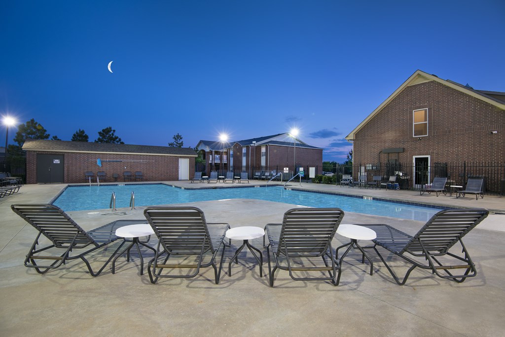our apartments at night with a pool and chairs