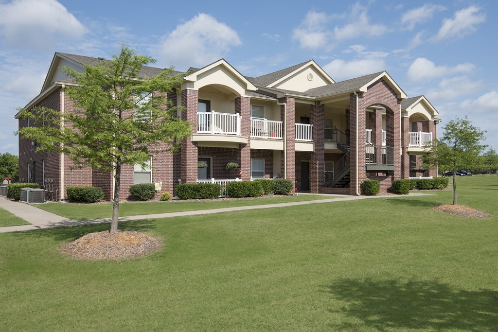 A large brick building with a balcony and a tree in front.