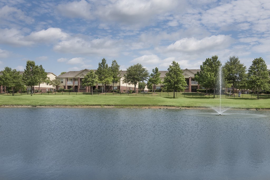 a fountain is in the middle of a pond in front of some apartments