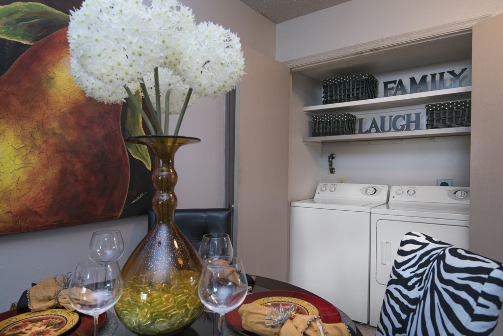 A vase with white flowers sits on a table next to wine glasses.