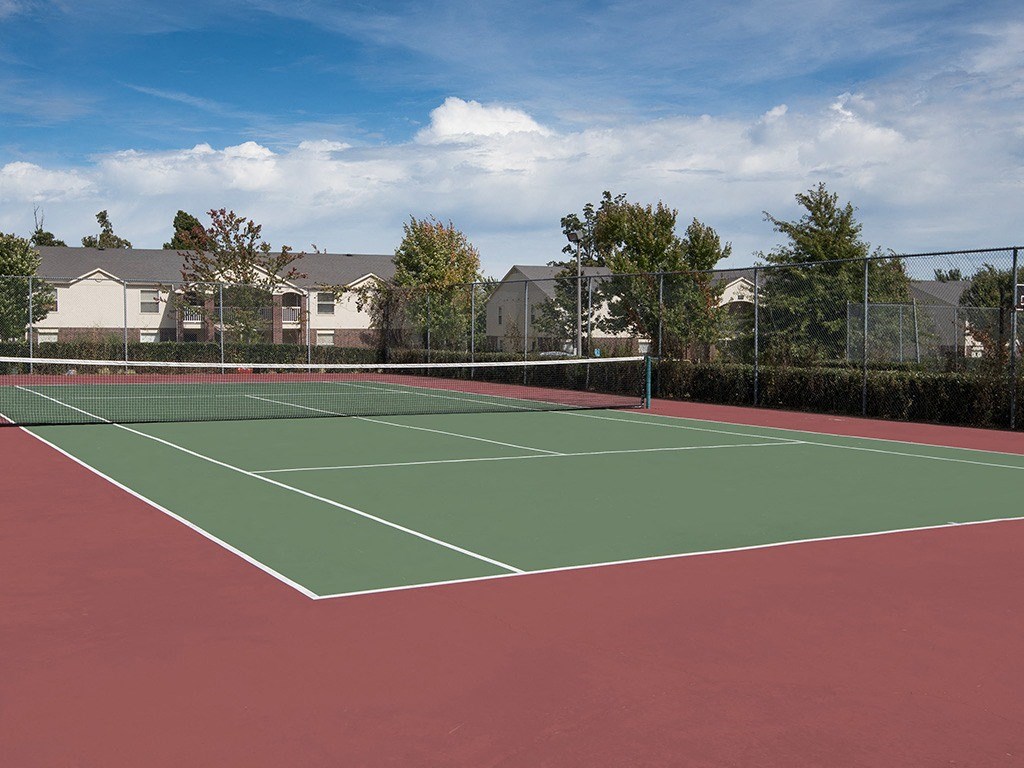 a tennis court with a fence and houses in the background