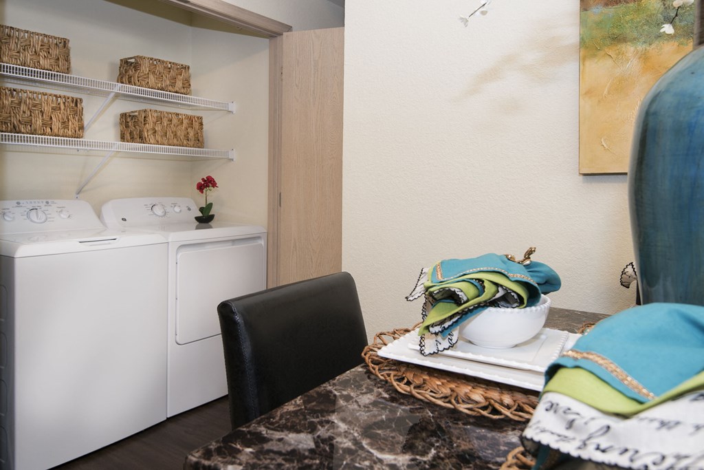 A laundry room with a washer and dryer, a black chair, and a table with a bowl and a bag on it.