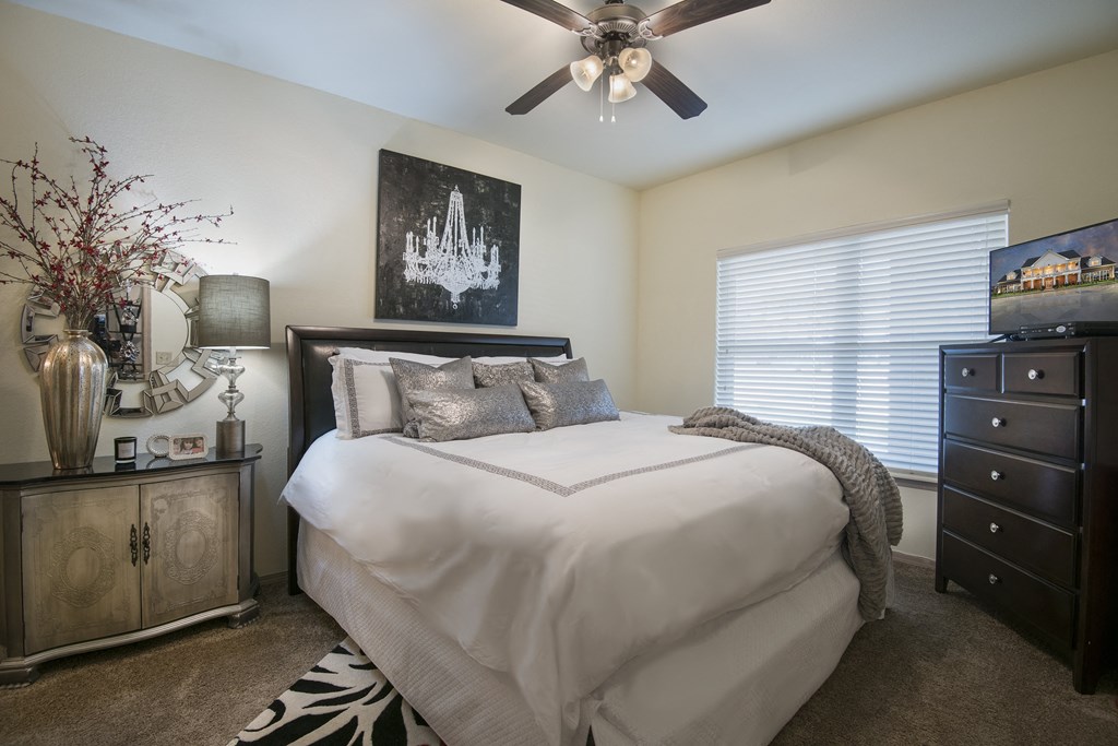 A bedroom with a large bed, a ceiling fan, and a dresser.