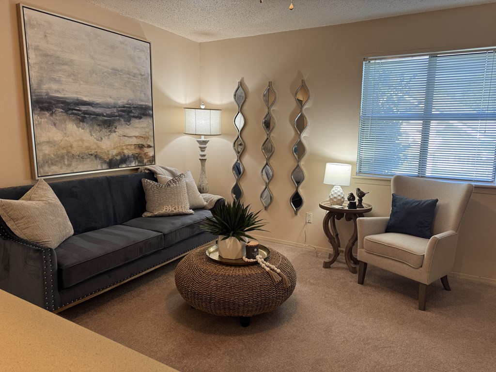 A living room with a grey couch, a wicker table, and a painting on the wall.