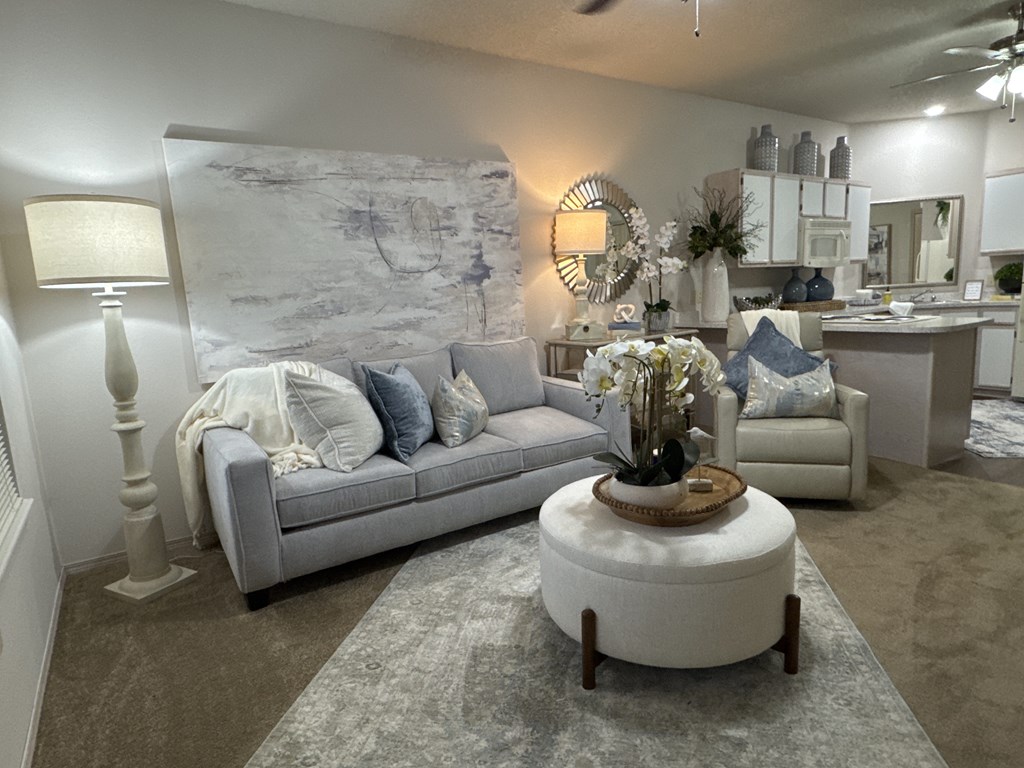 A living room with a grey couch, a round ottoman, and a large mirror on the wall.