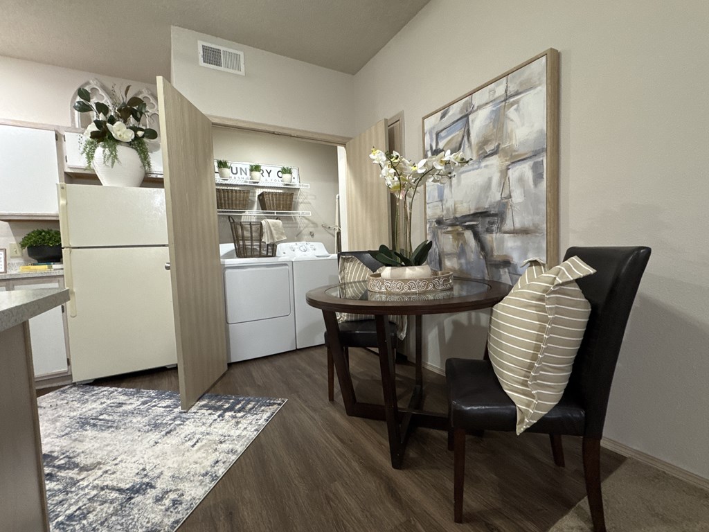 A kitchen with a table and chairs in the foreground and a refrigerator with a sign that says "UNITY" on it in the background.