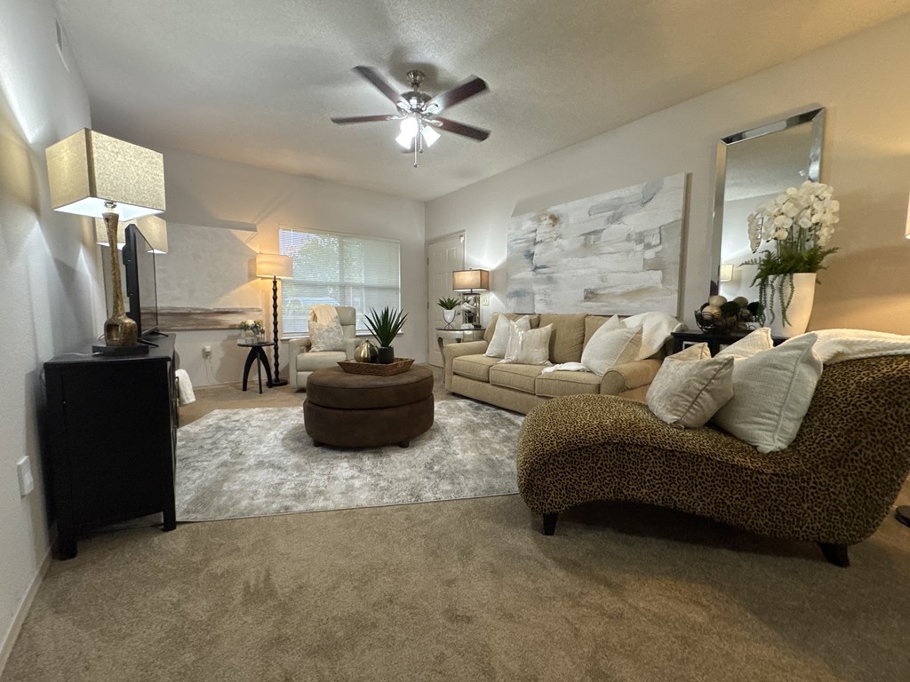 A living room with a brown couch, a brown ottoman, and a ceiling fan.
