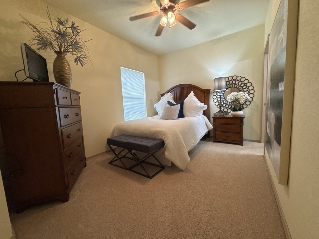 A bedroom with a bed, dresser, and ceiling fan.