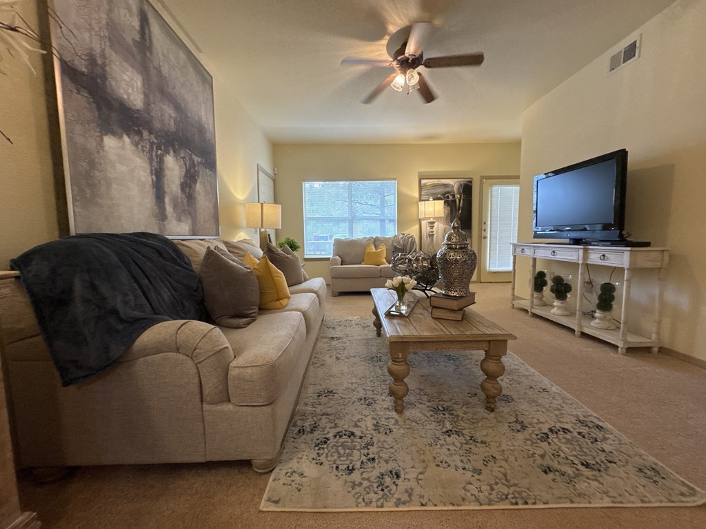 A living room with a beige couch, a rug, and a ceiling fan.