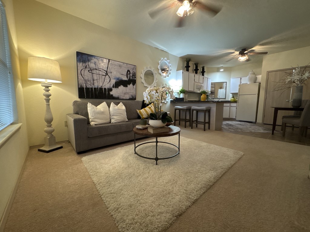 A living room with a grey couch, a white rug, and a ceiling fan.