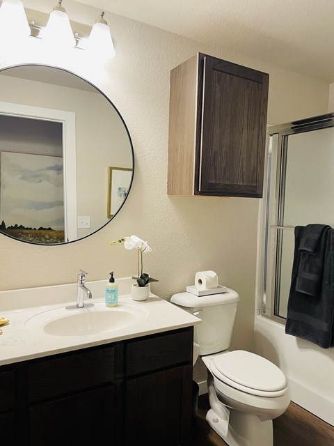 A bathroom with a toilet, sink, mirror, and a towel hanging on the door.