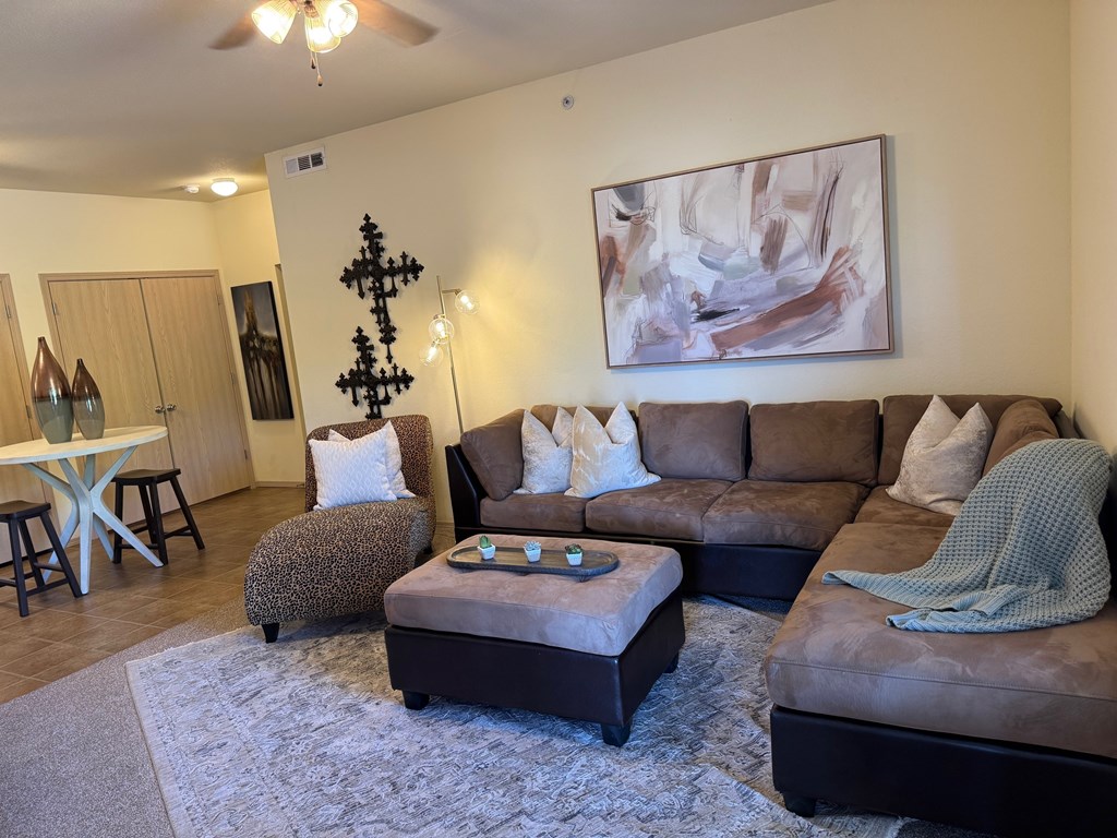 A living room with a brown couch, a grey ottoman, and a painting on the wall.