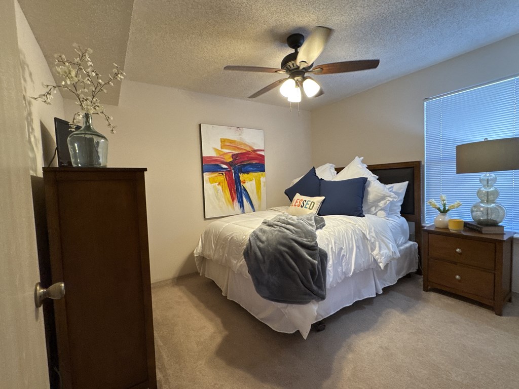 A bedroom with a bed, a ceiling fan, and a painting on the wall.