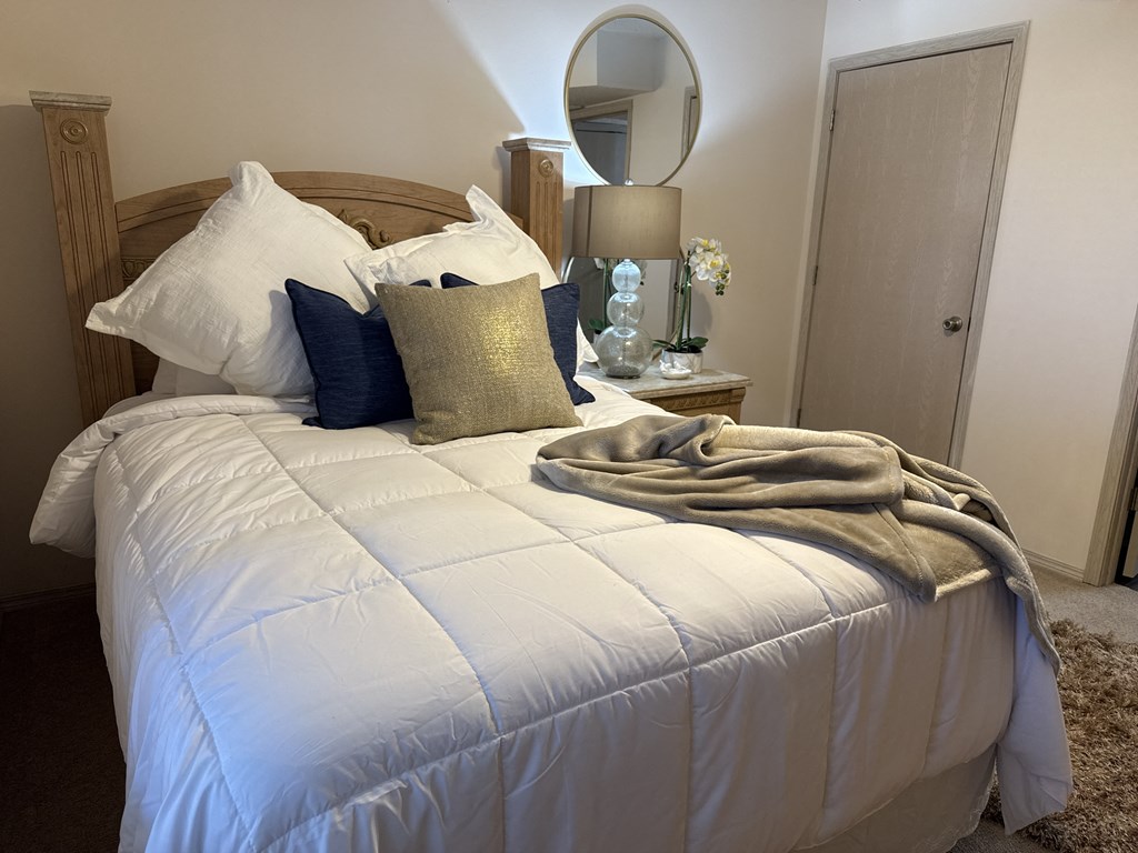 A bed with a white comforter and a brown blanket.