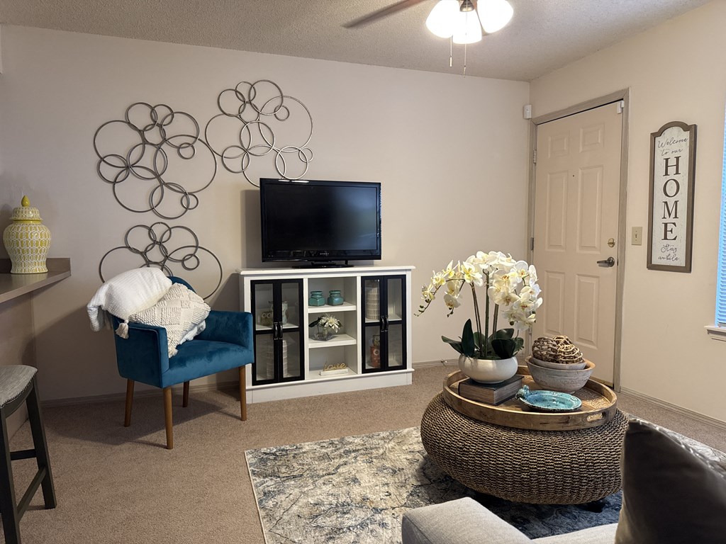 A living room with a television, a chair, a table, and a wall art.