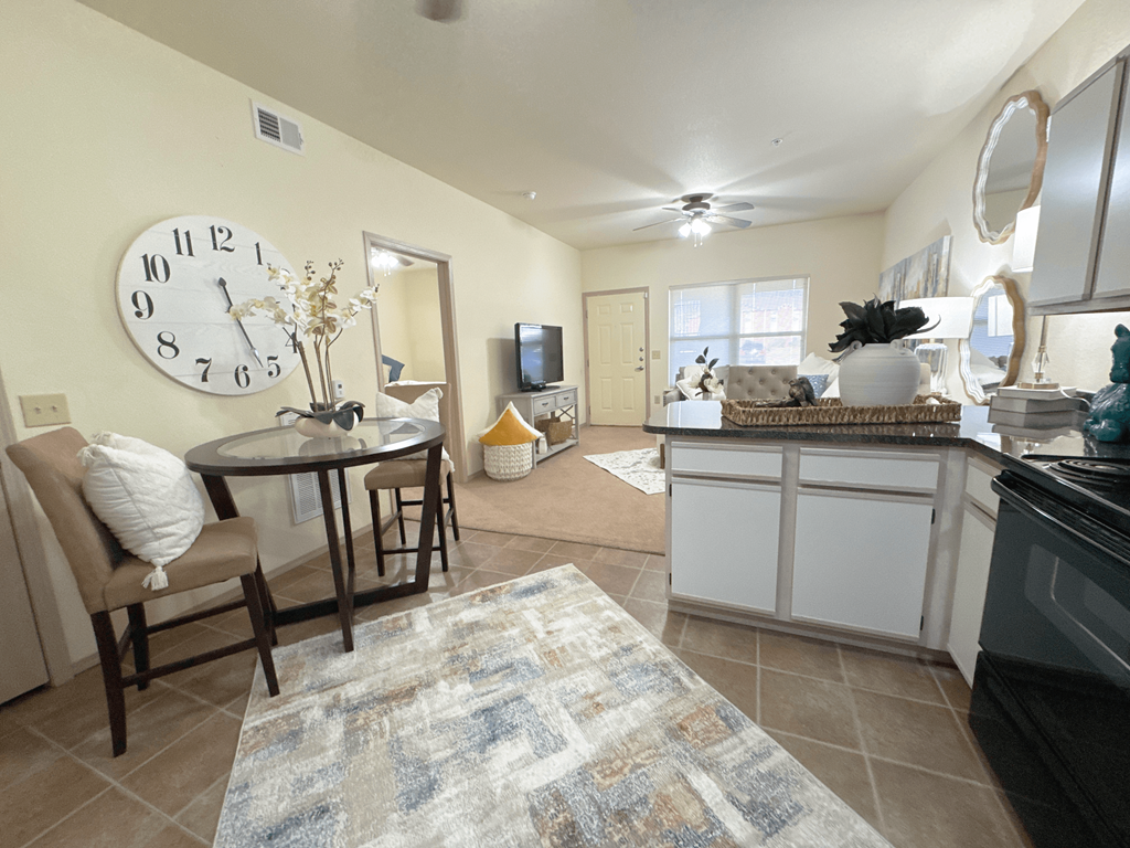 A kitchen with a table and chairs in the foreground and a clock on the wall.