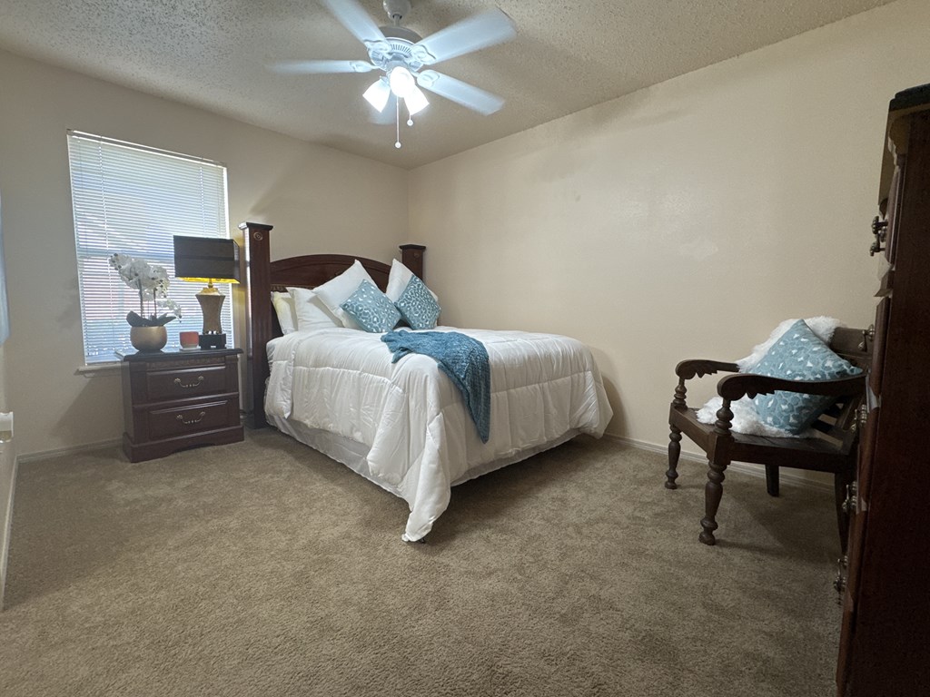 A bedroom with a bed, chair, and ceiling fan.