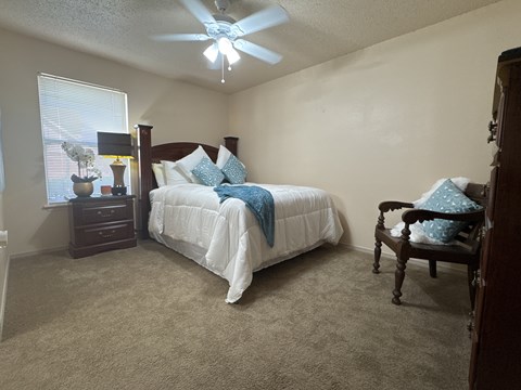 A bedroom with a bed, chair, and ceiling fan.