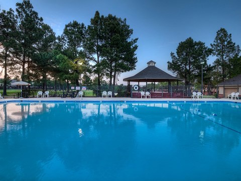 A pool with a gazebo and trees in the background.
