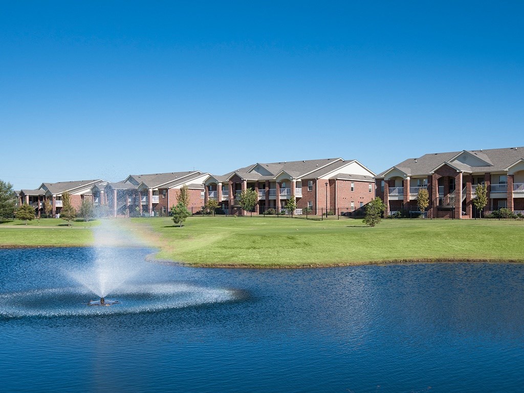 A fountain in the middle of a lake in front of a row of houses.