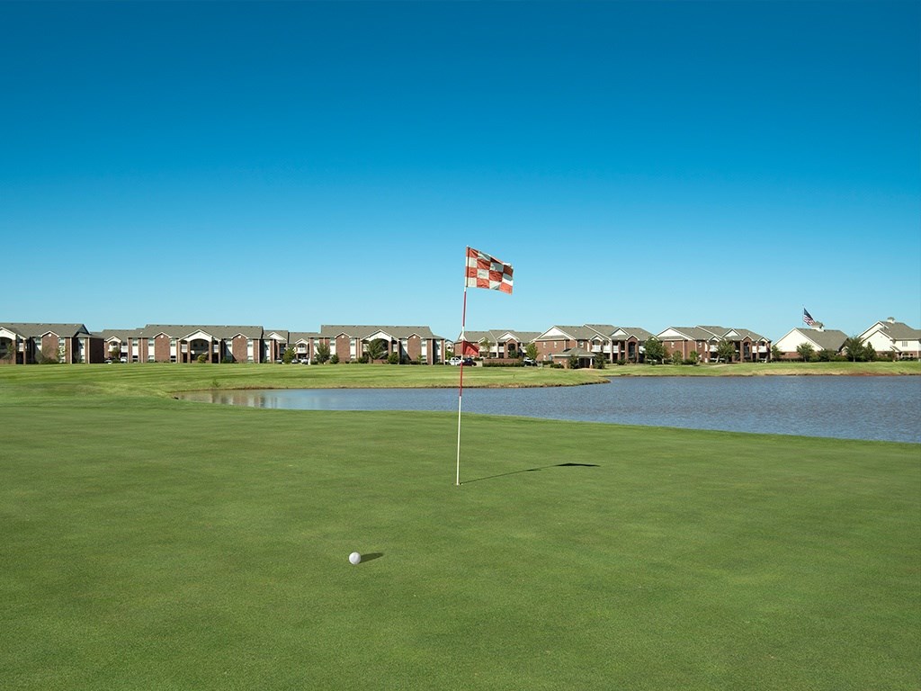 A golf course with a hole in the foreground and a flag on a pole.