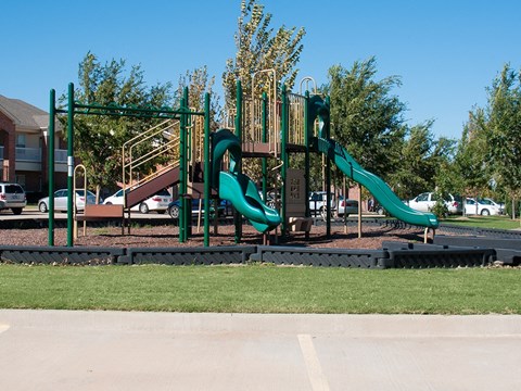 A playground with a green slide and a brown wooden structure.