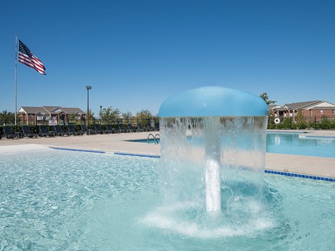 A water fountain in the middle of a pool with an American flag in the background.