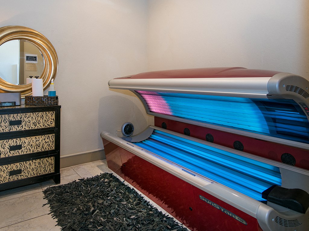 A tanning bed with a red light on the right side and a black and gold cabinet on the left.