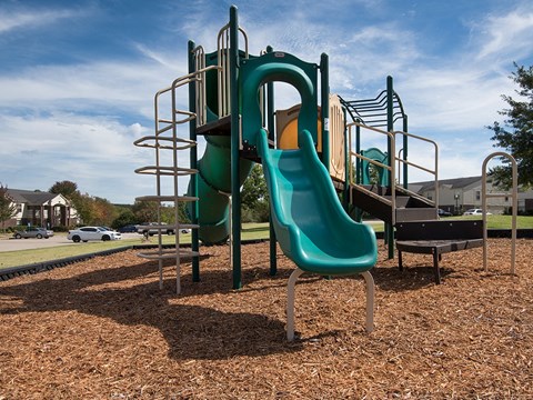 a playground with a slide and chairs in a park