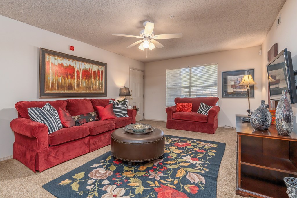 a living room with red couches and a rug and a ceiling fan